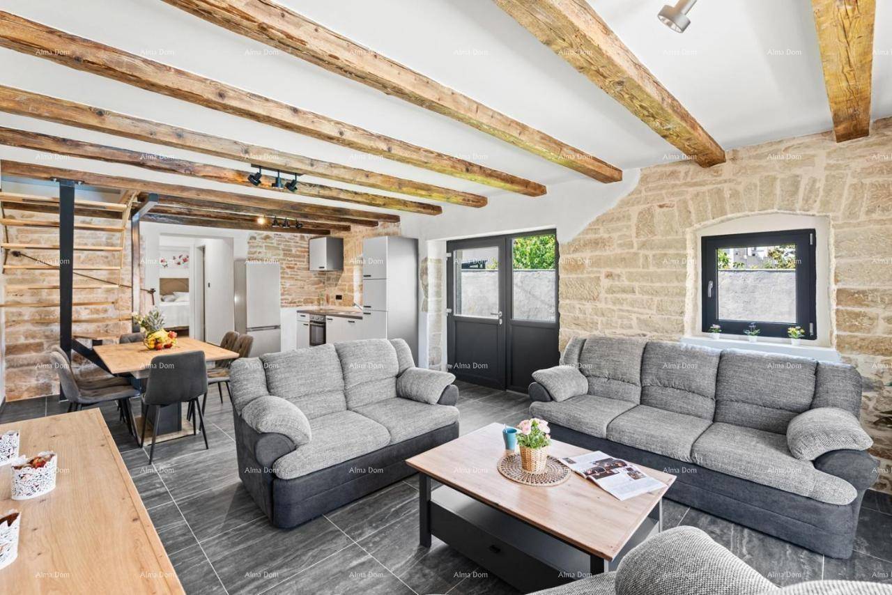 Heller Wohn-Essbereich mit grauen Sofas, Holzbalken und Blick auf die moderne Küche und die offene Treppe.