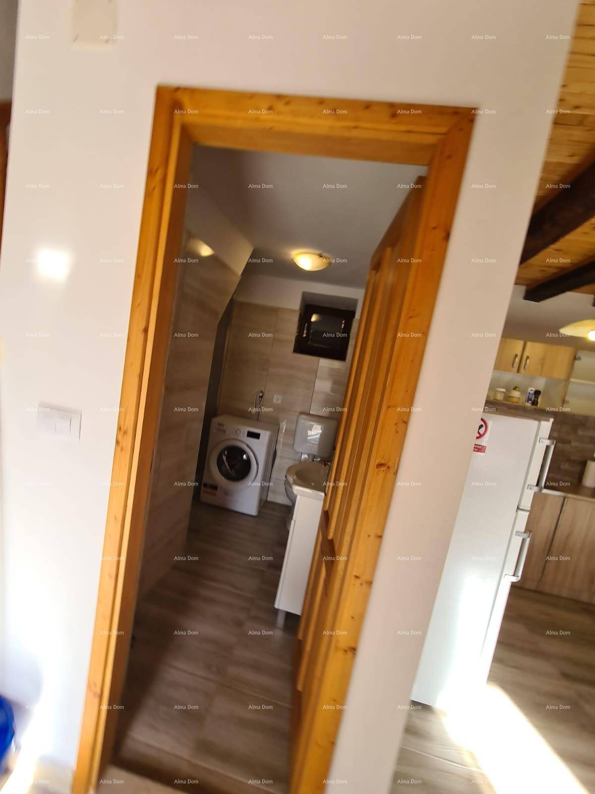 Badezimmer mit Waschmaschine, Toilette und Waschbecken, sichtbar durch eine offene Holztür vom Flur.