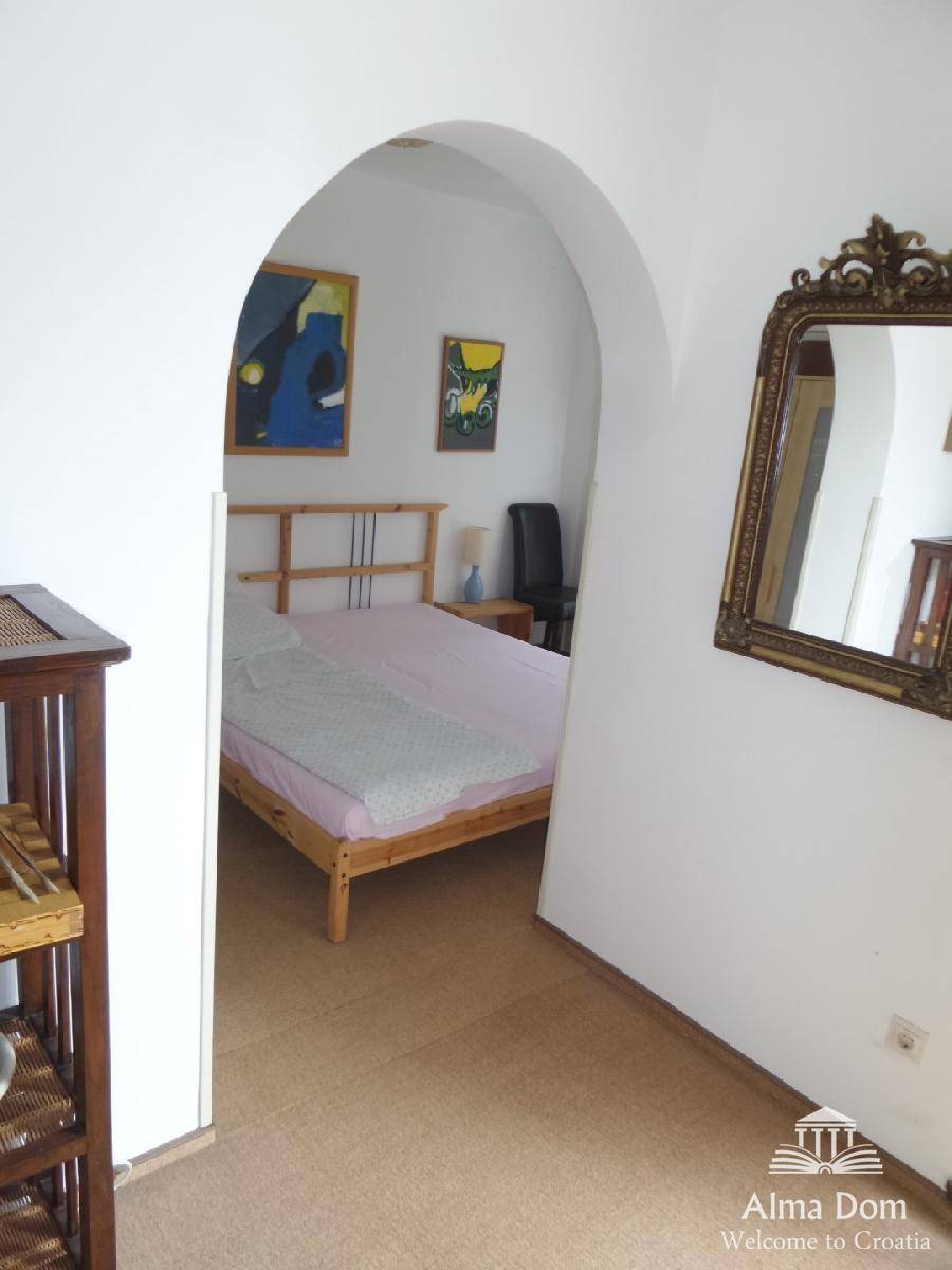 Schlafzimmer mit Holzbett und gewölbtem Durchgang, dekoriert mit Kunstwerken, schlicht und funktional.