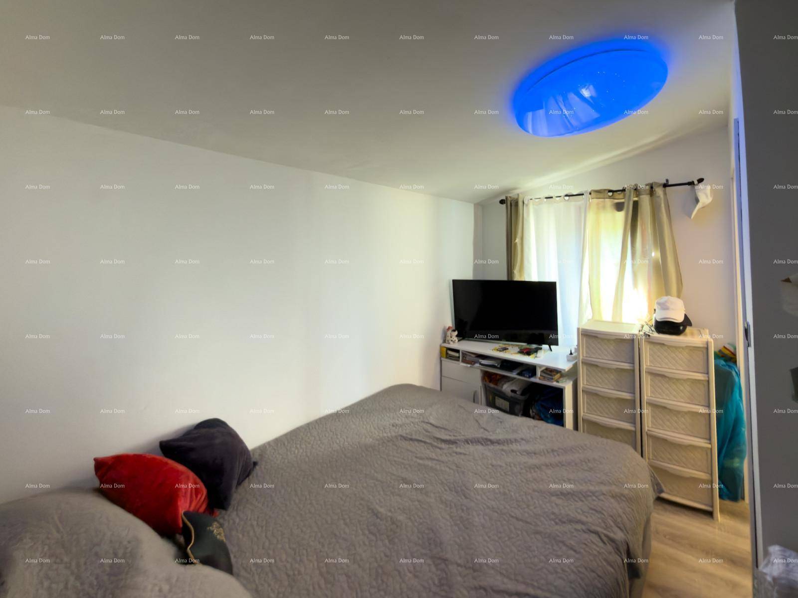 Helles Schlafzimmer mit Doppelbett, Fernseher und Fenster mit Vorhängen.