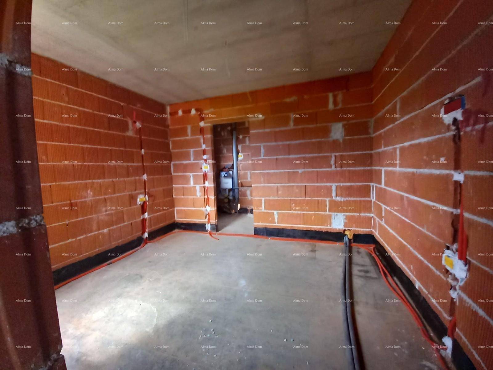Innenraum im Rohbau mit unverputzten Ziegelwänden und sichtbaren Elektroinstallationen.