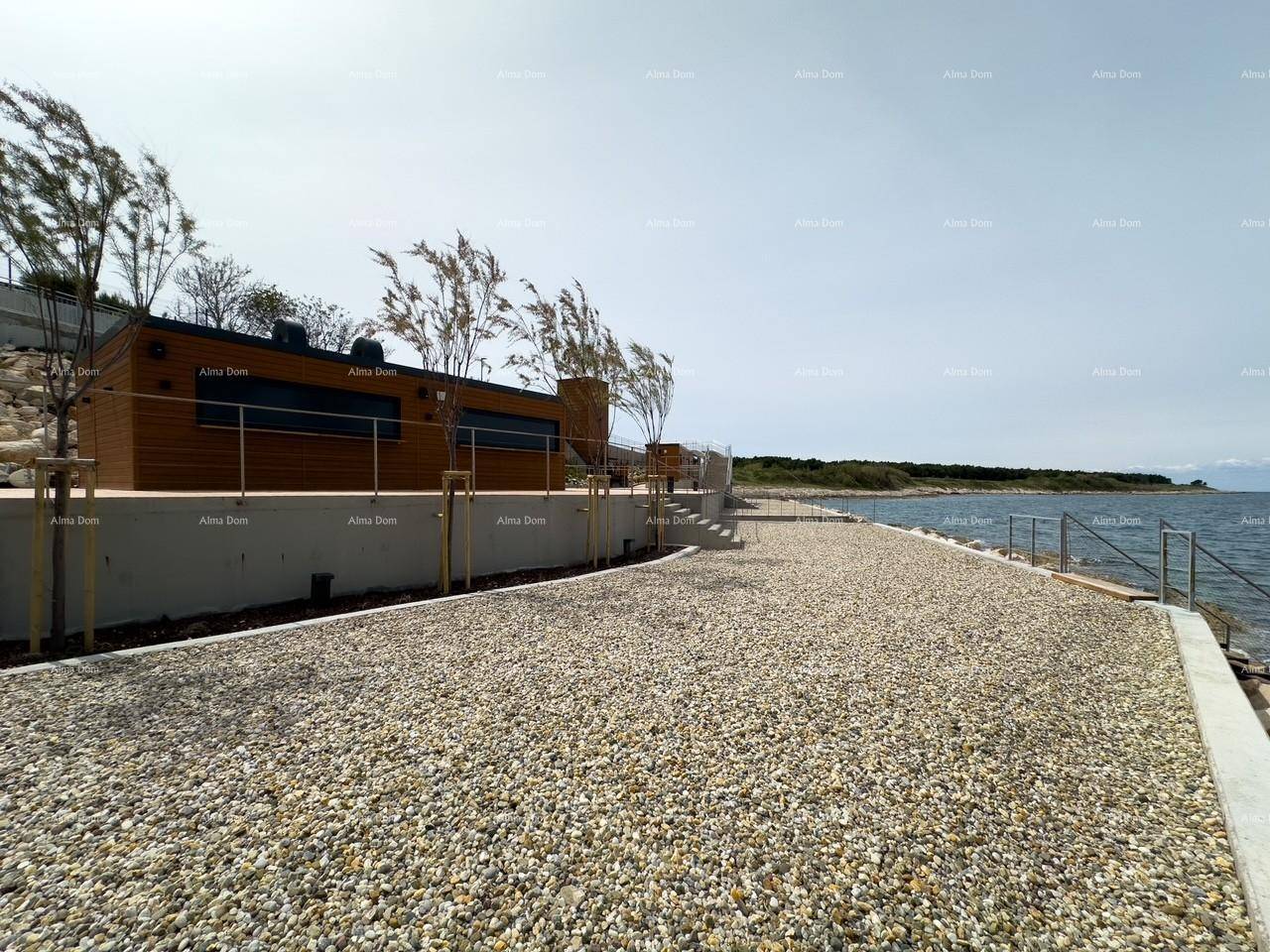 Kiesweg entlang der Küste mit Blick auf das Meer und moderne Gebäude im Hintergrund.