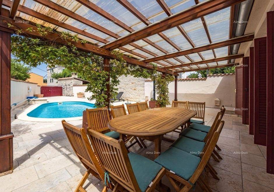 Überdachte Terrasse mit Holztisch und Stühlen, umgeben von Pflanzen und Blick auf den Pool.