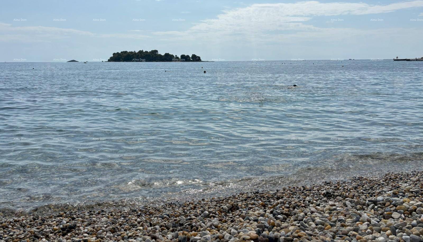 Klares Meerwasser mit einem kleinen Inselchen in der Ferne und einem Kiesstrand im Vordergrund.