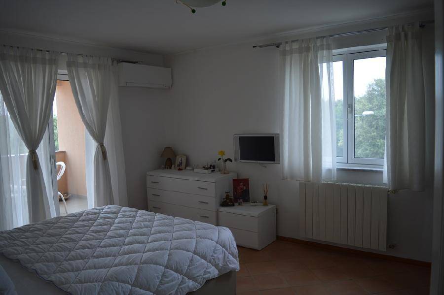 Helles Schlafzimmer mit Doppelbett, Kommode, Klimaanlage und Zugang zum Balkon.