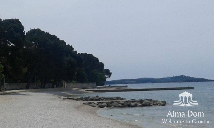 Langer Kiesstrand mit Felsen und einem Pier, umgeben von Bäumen und Meer, weitläufig und natürlich.