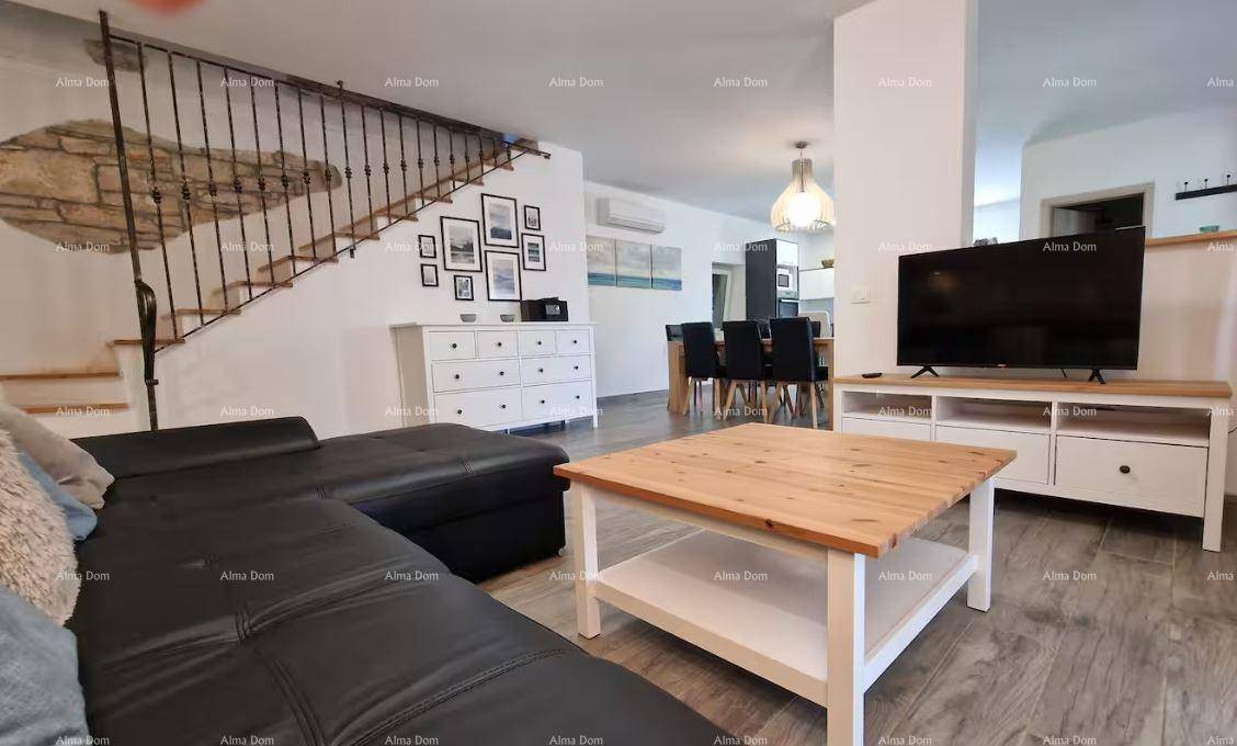 Helles Wohnzimmer mit Ledersofa, Fernseher und Treppe mit schmiedeeisernem Geländer.