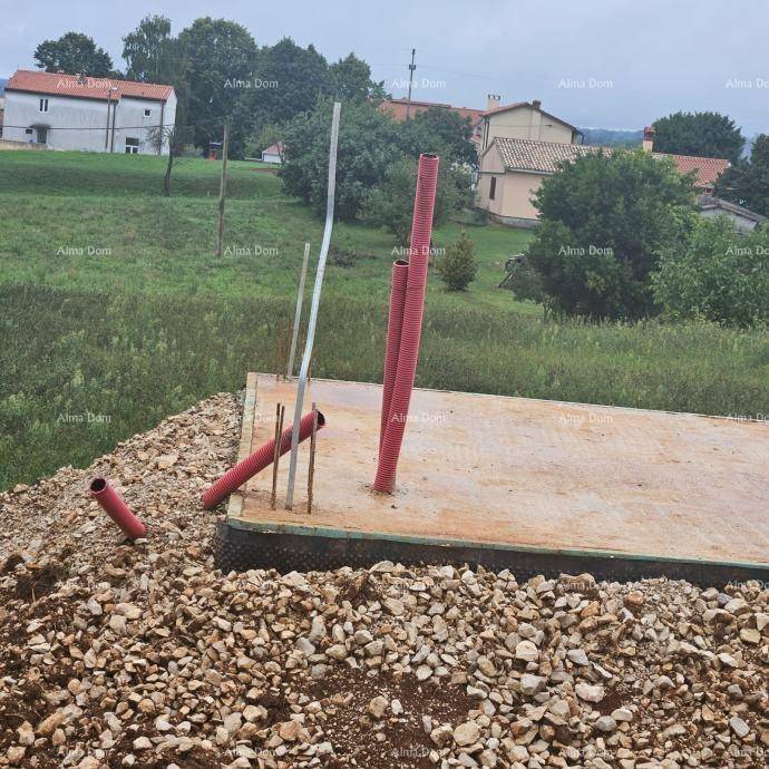 Betonfundament mit roten Rohren und Bewehrungsstäben, umgeben von Schotter und ländlicher Umgebung.