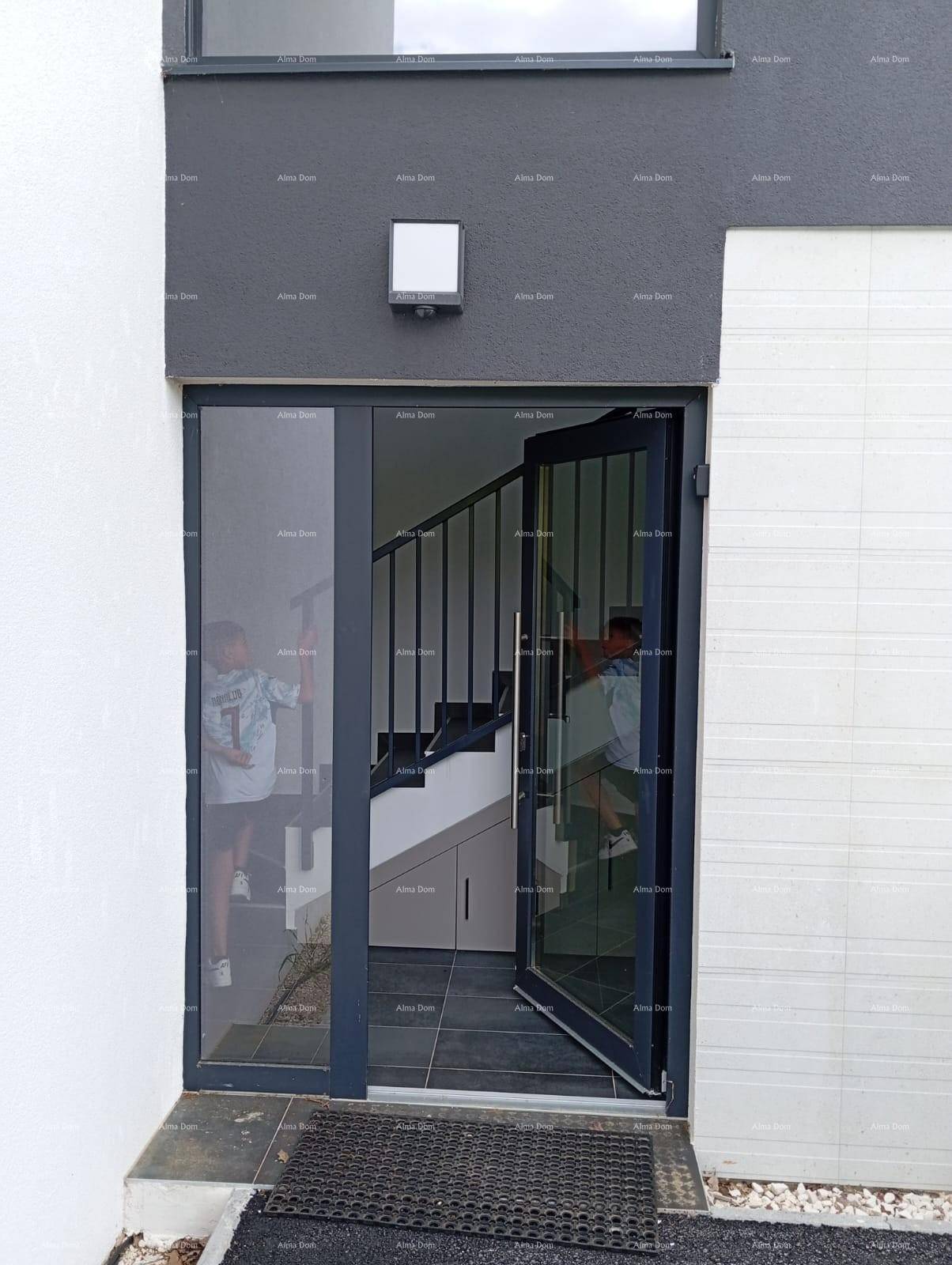 Moderner Eingangsbereich mit dunkler Fassade und einer Glastür, die den Blick auf eine Treppe freigibt.