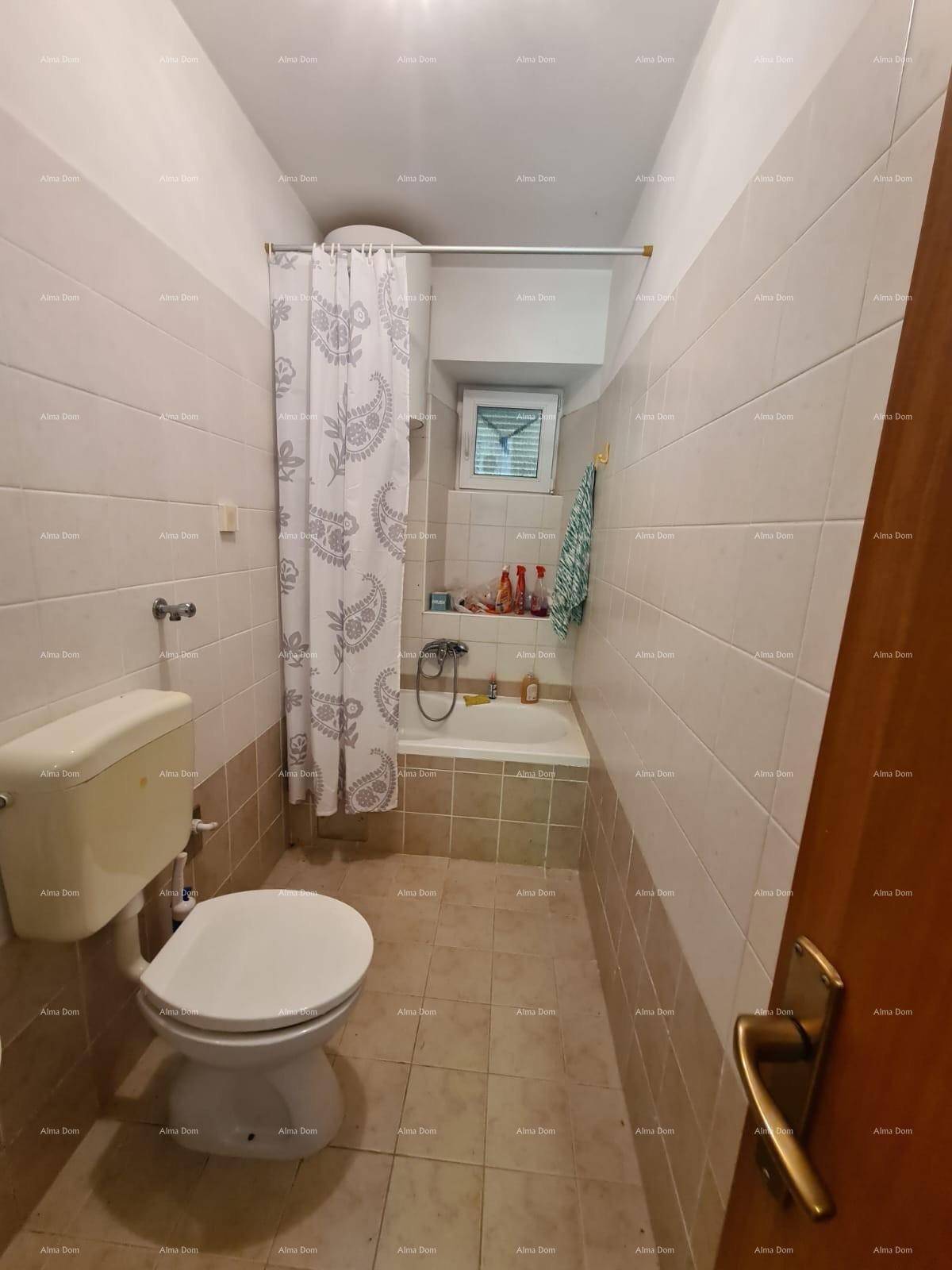 Badezimmer mit Toilette und Badewanne mit Duschvorhang, hell gefliest und mit kleinem Fenster.