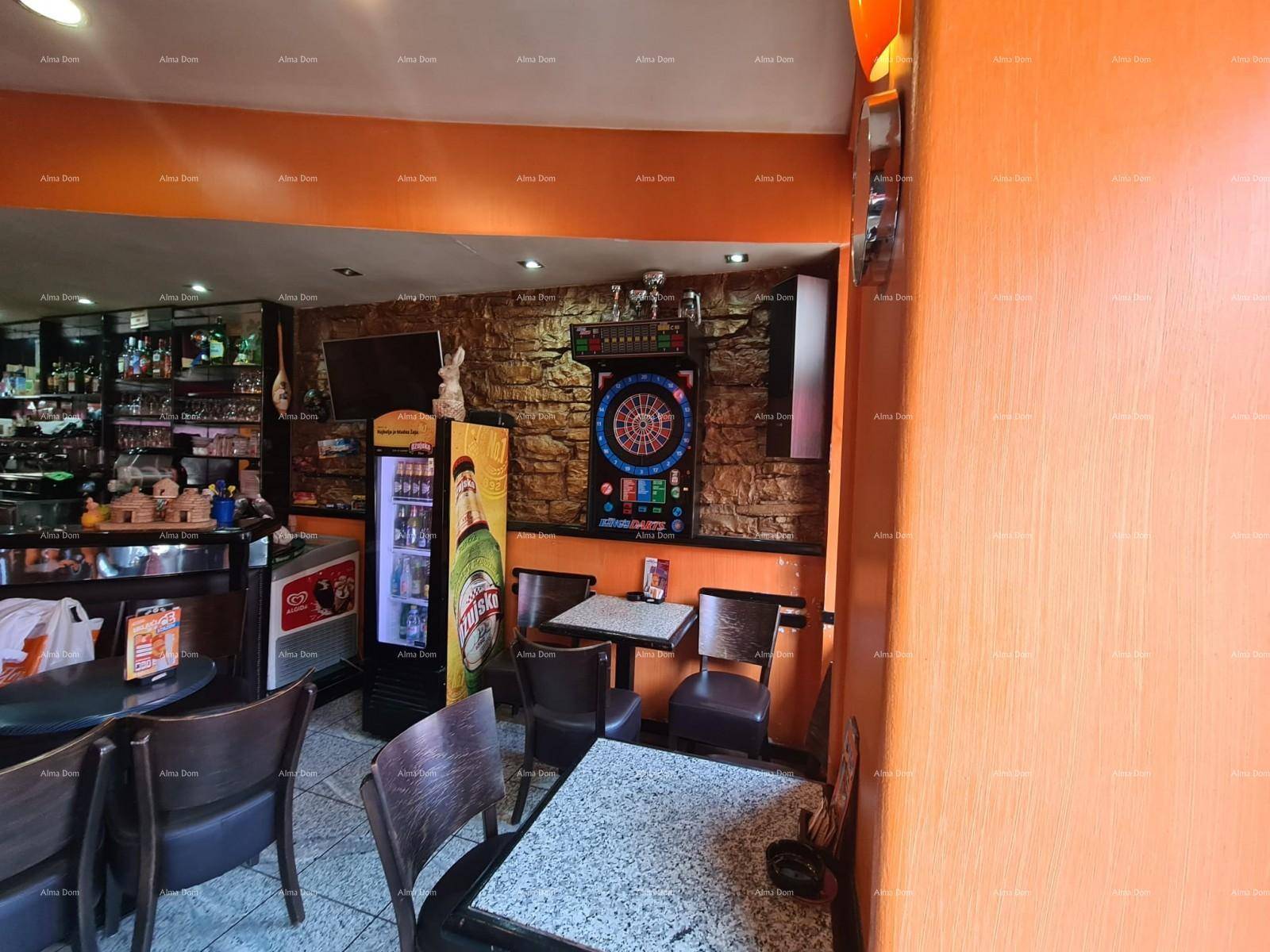 Innenansicht einer Bar mit Sitzgelegenheiten, einem Kühlschrank und einem Dartboard an einer strukturierten Wand.