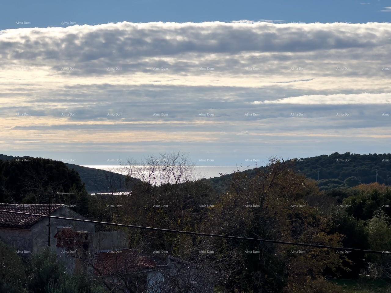 Weiter Blick über die hügelige Landschaft bis zum Meer unter einem bewölkten Himmel.