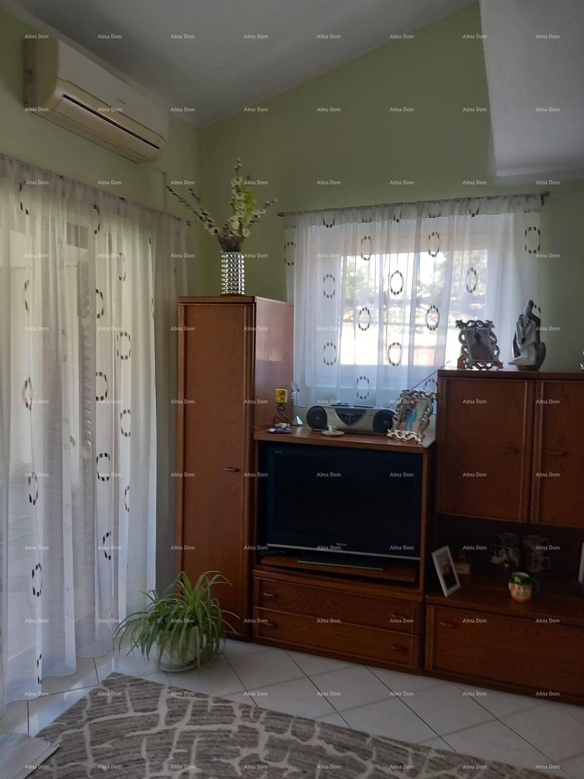 Wohnzimmer mit Holzmöbeln, Fernseher und Klimaanlage, auf einem Fliesenboden.