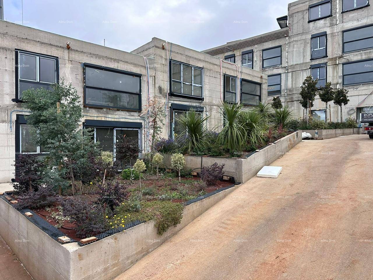 Moderne Gebäudefassade mit großen Fenstern und einem frisch angelegten Gartenbereich mit Sträuchern.