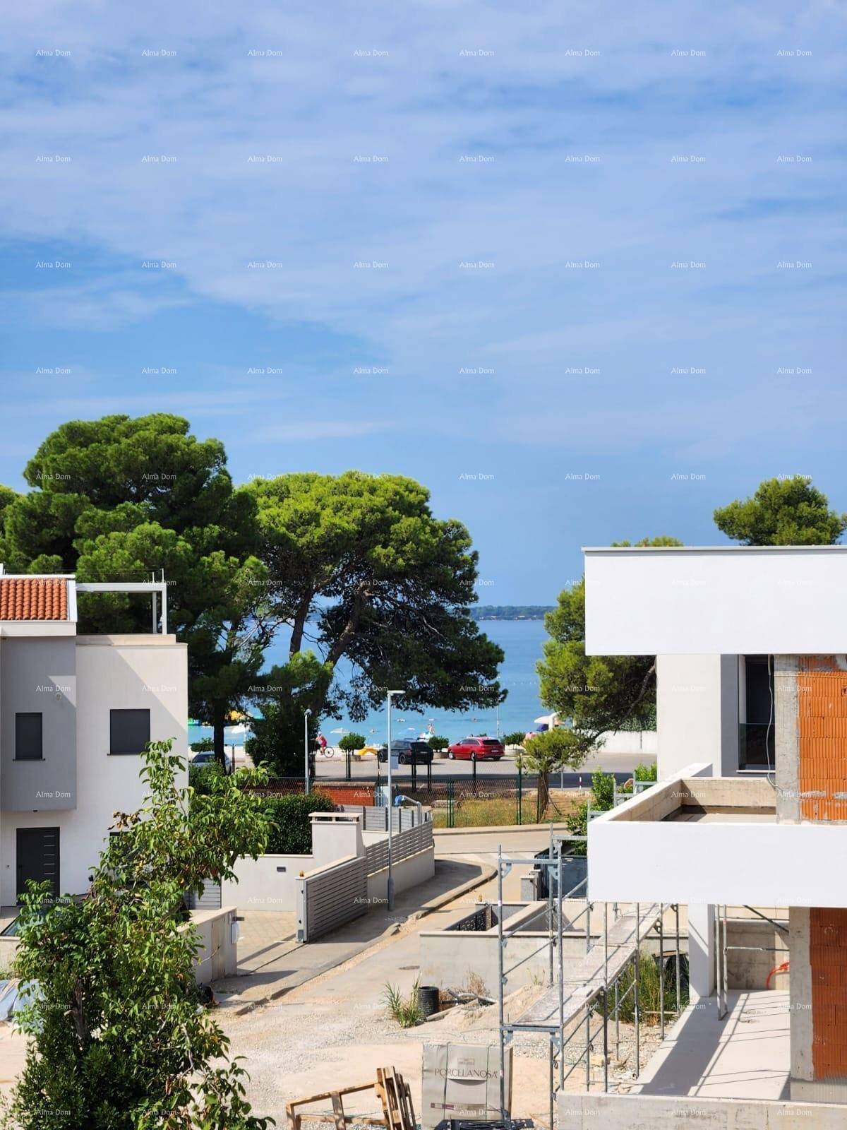 Blick von der Baustelle auf das Meer, umgeben von grünen Bäumen und weiteren Gebäuden.