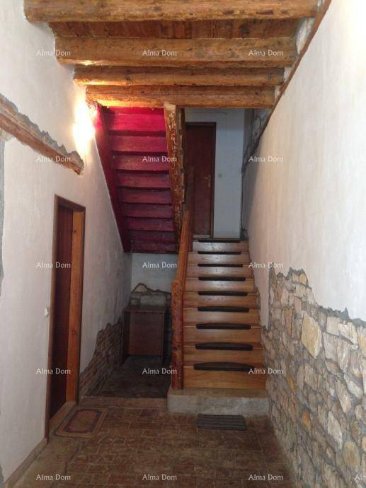 Treppenhaus mit Holztreppe, freiliegenden Holzbalken und Steinwand.