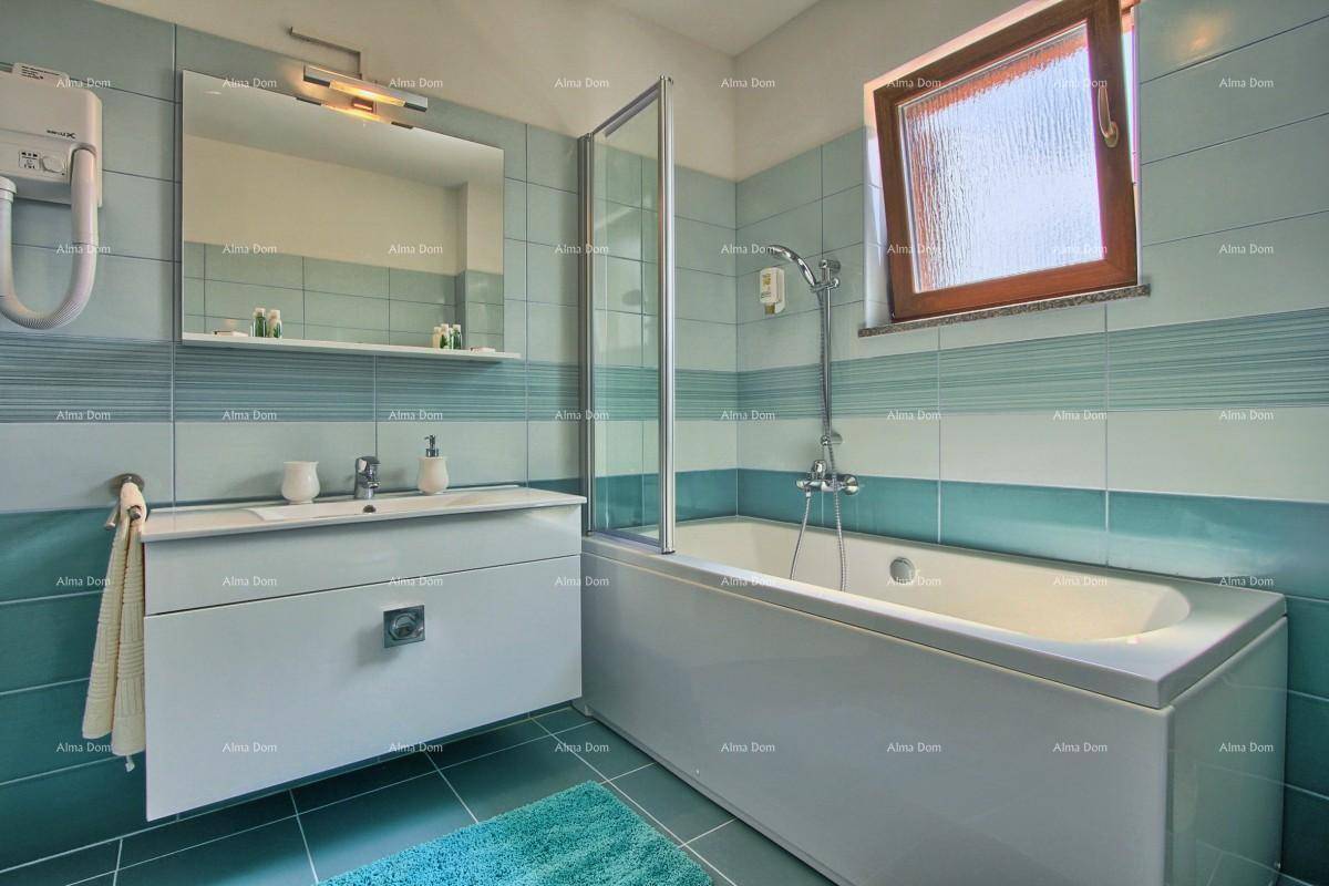 Badezimmer mit blauen und grünen Fliesen, Badewanne mit Duschwand und Fenster.