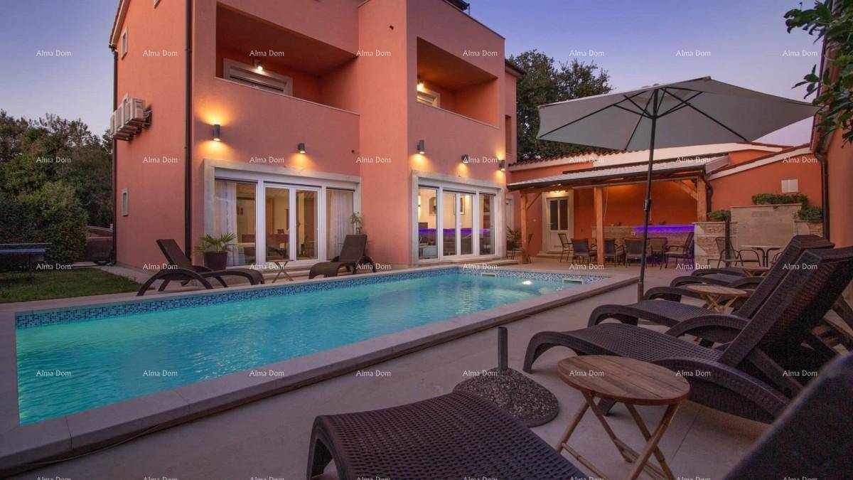 Abendliche Ansicht des Pools mit beleuchteter Fassade, Liegestühlen und Sonnenschirm.
