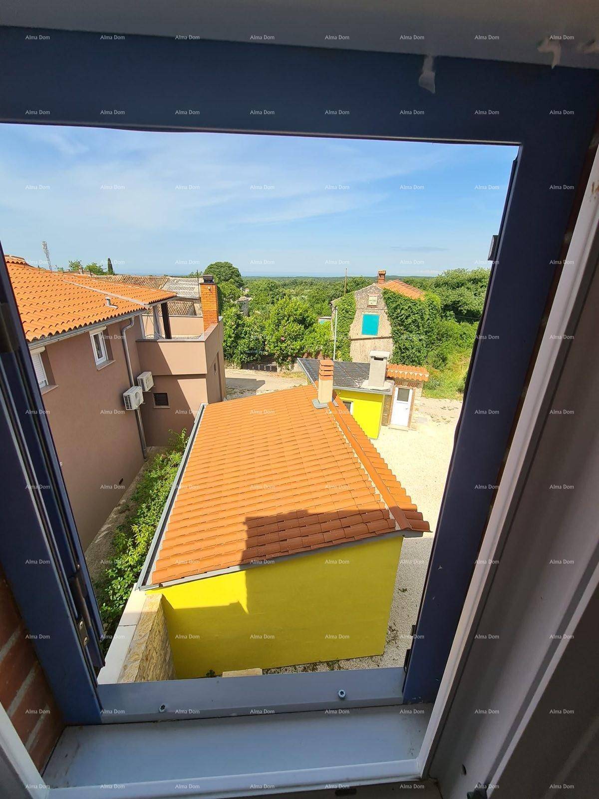 Ausblick aus dem Fenster auf umliegende Dächer, ein gelbes Gebäude und die Landschaft.