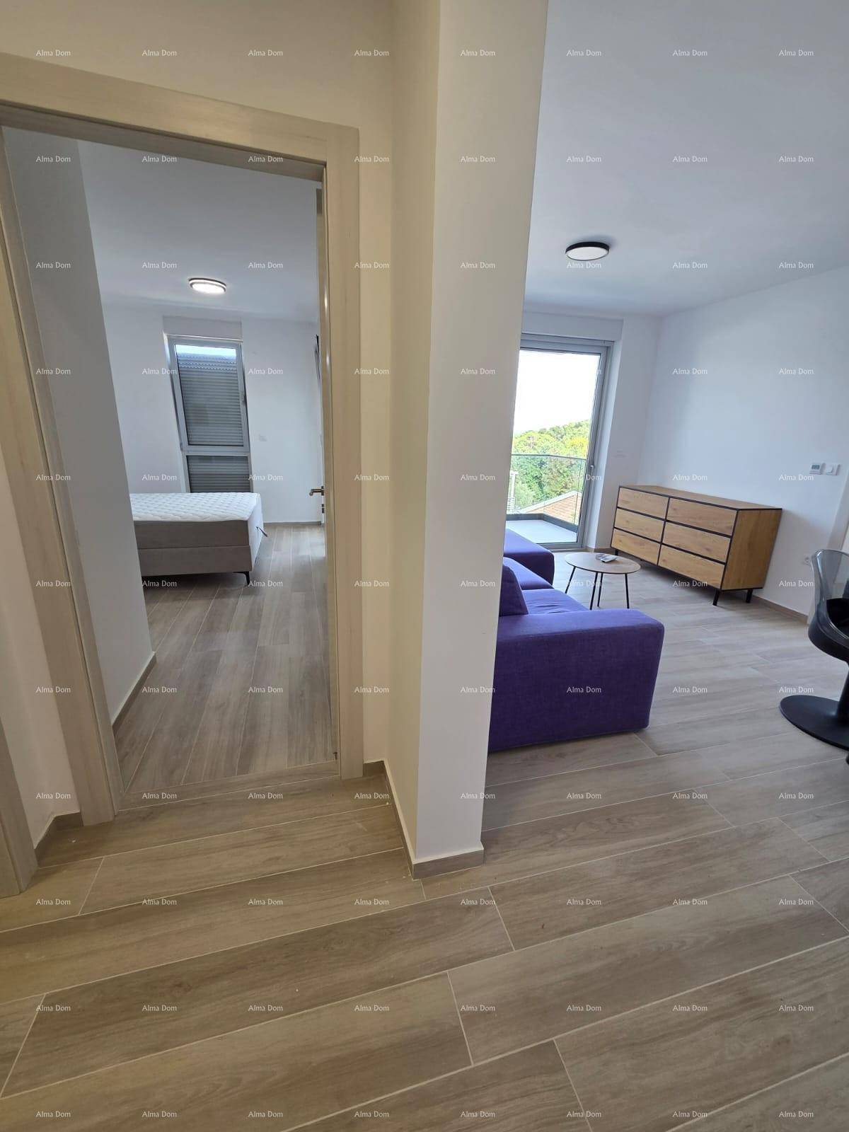 Offener Wohnbereich mit lila Sofa, Fliesenboden und Zugang zu einem Schlafzimmer und Balkon.