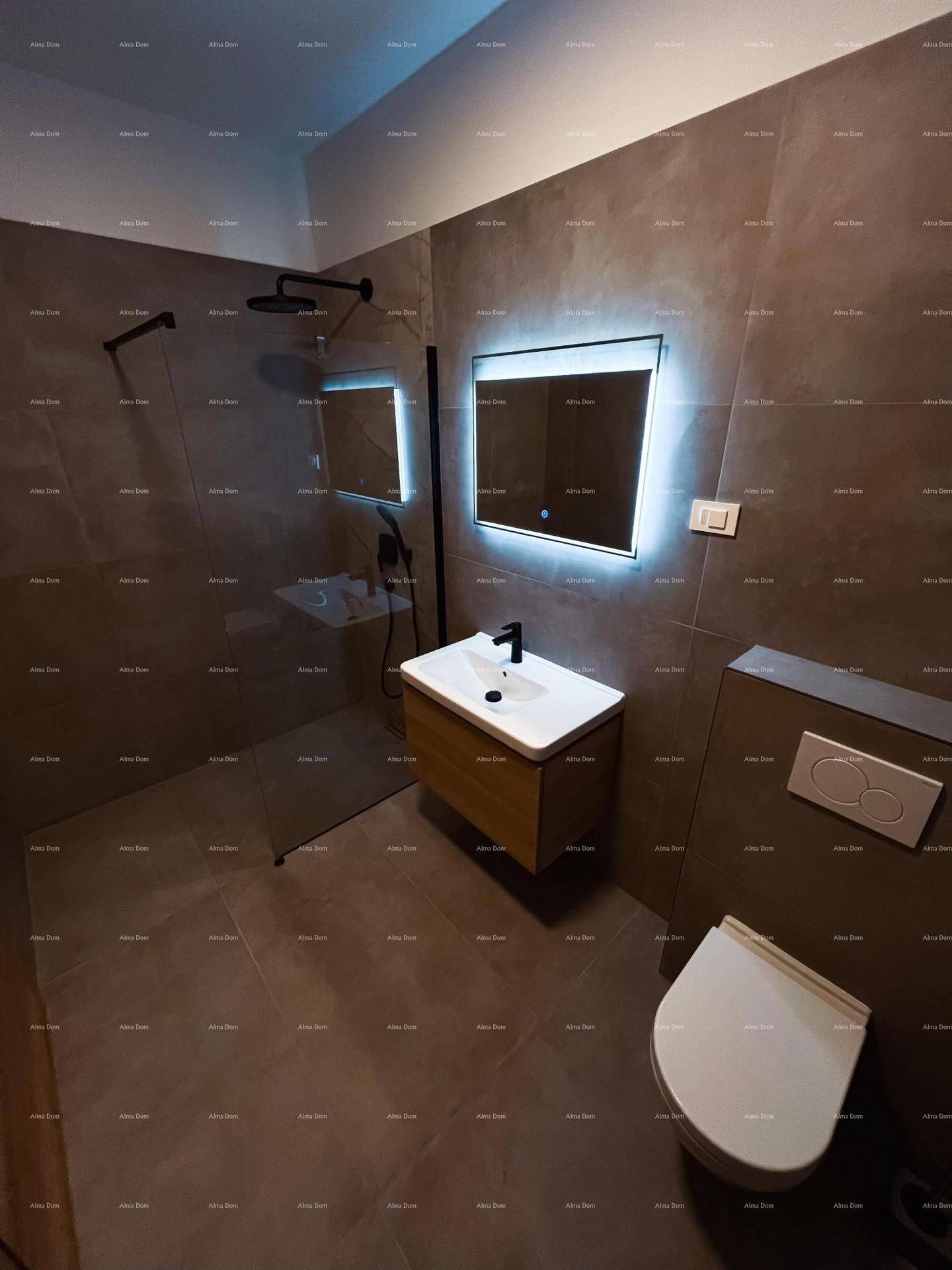 Modernes Badezimmer mit grauen Fliesen, schwebendem Waschtisch, beleuchtetem Spiegel und Duschbereich.