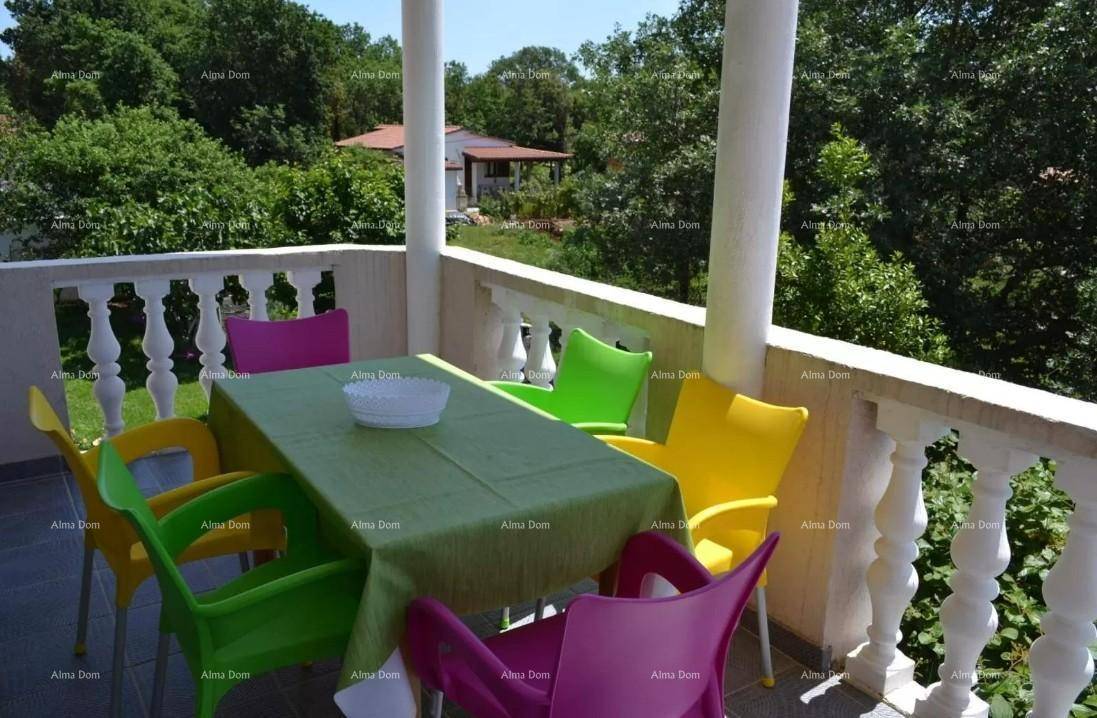 Überdachter Balkon mit bunten Stühlen und Tisch, umgeben von üppigem Grün.