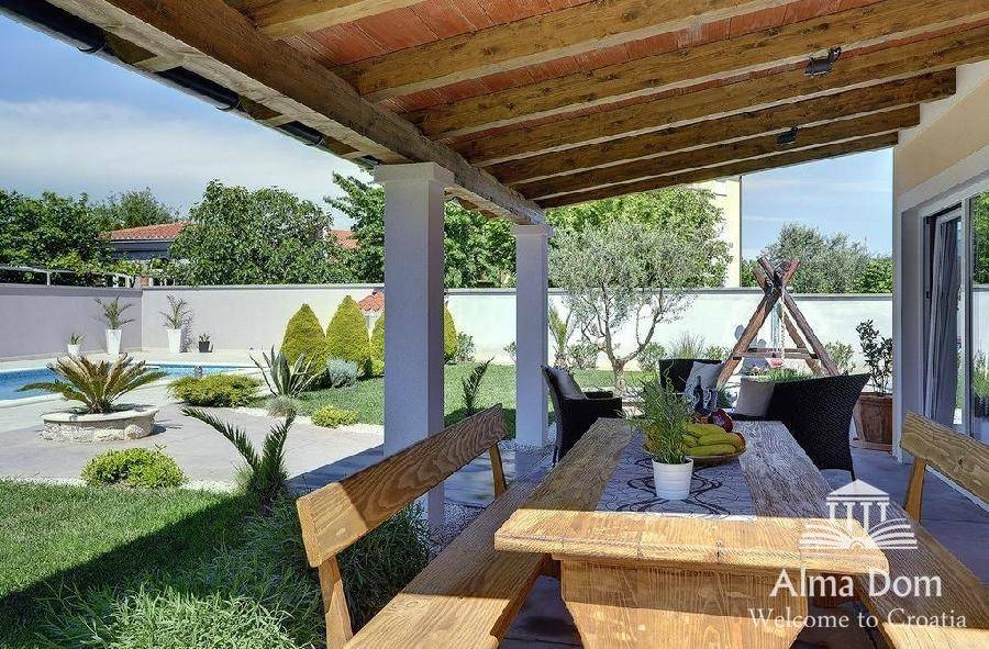 Rustikaler Essbereich unter einer überdachten Terrasse mit Holzbalken und Gartenblick.