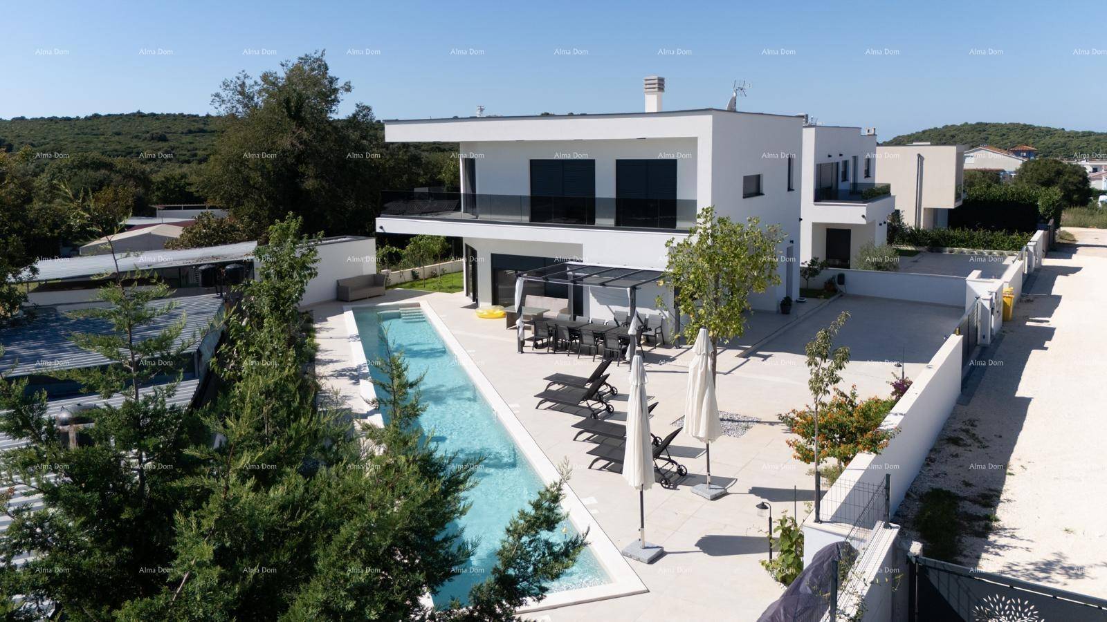 Moderne Villa mit langem Pool, Sonnenliegen und gepflegter Außenanlage unter blauem Himmel.