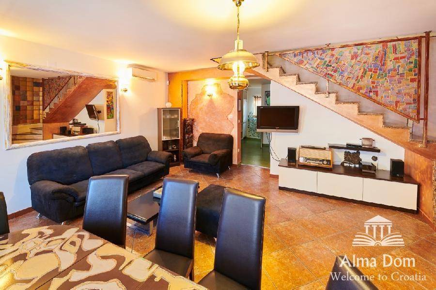 Wohn- und Essbereich mit Esstisch, Sofas und einer kunstvoll gestalteten Treppe.