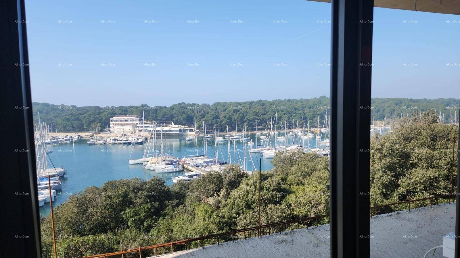 Panoramaaussicht auf den Yachthafen und die grüne Küste durch eine breite Fensterfront.