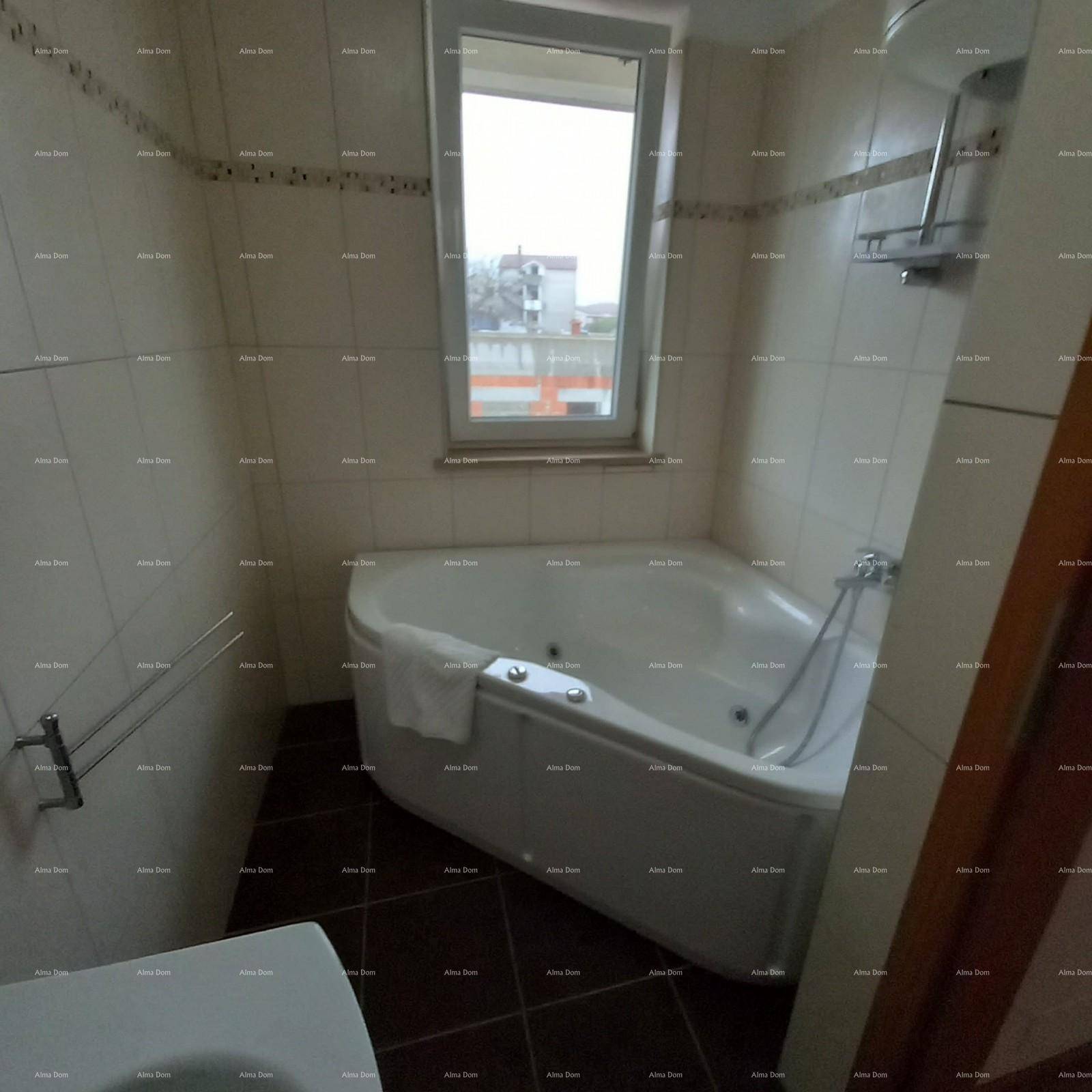 Badezimmer mit Eckbadewanne, Fenster und Fliesen an Wänden und Boden.