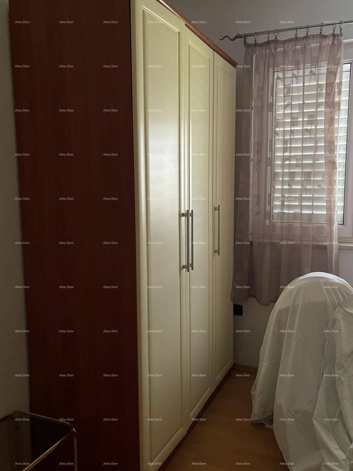 Schlafzimmer mit einem großen Kleiderschrank, hellem Holzfußboden und einem Fenster mit Vorhängen.