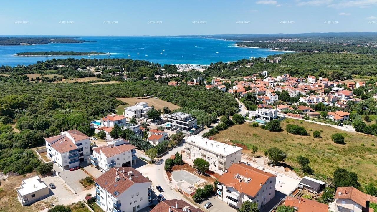 Luftaufnahme einer Küstensiedlung mit Wohngebäuden, viel Grün und dem Meer im Hintergrund unter blauem Himmel.