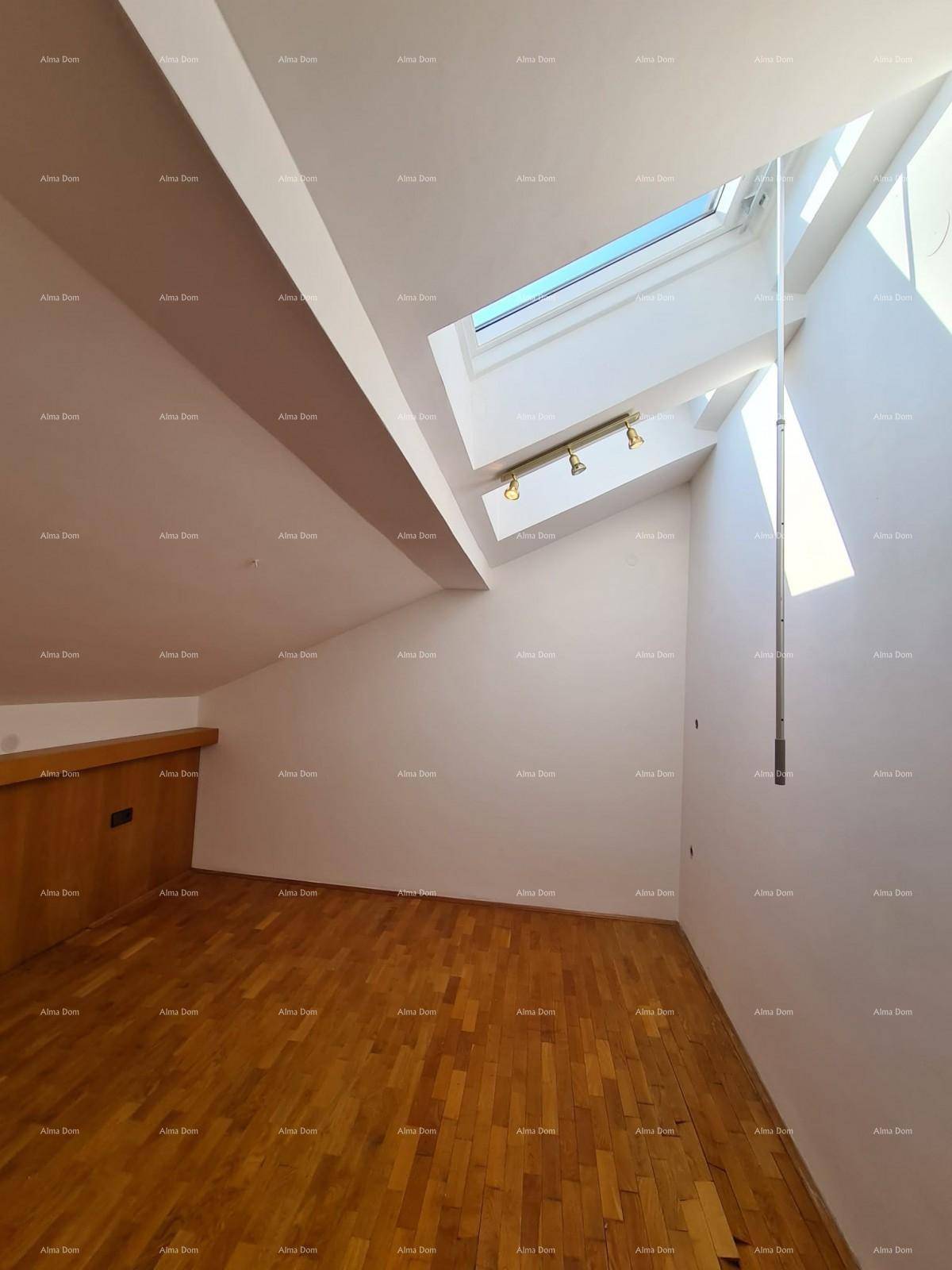 Helles Dachzimmer mit Holzparkettboden, schrägen Wänden und einem großen Dachfenster für viel Tageslicht.