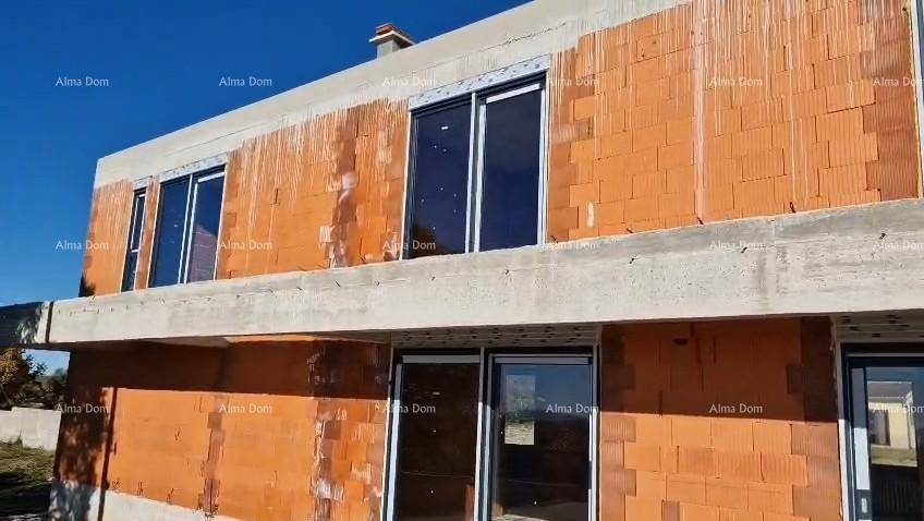 Vorderansicht des Rohbaus mit Ziegelwänden, Betonelementen und installierten Fenstern.