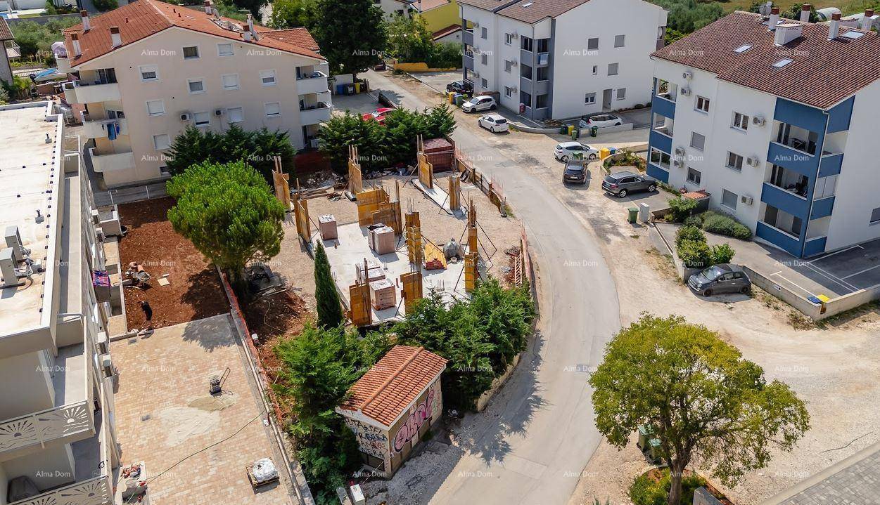 Luftaufnahme einer Baustelle mit Fundamentarbeiten, umgeben von Wohngebäuden und einem kleinen Schuppen.