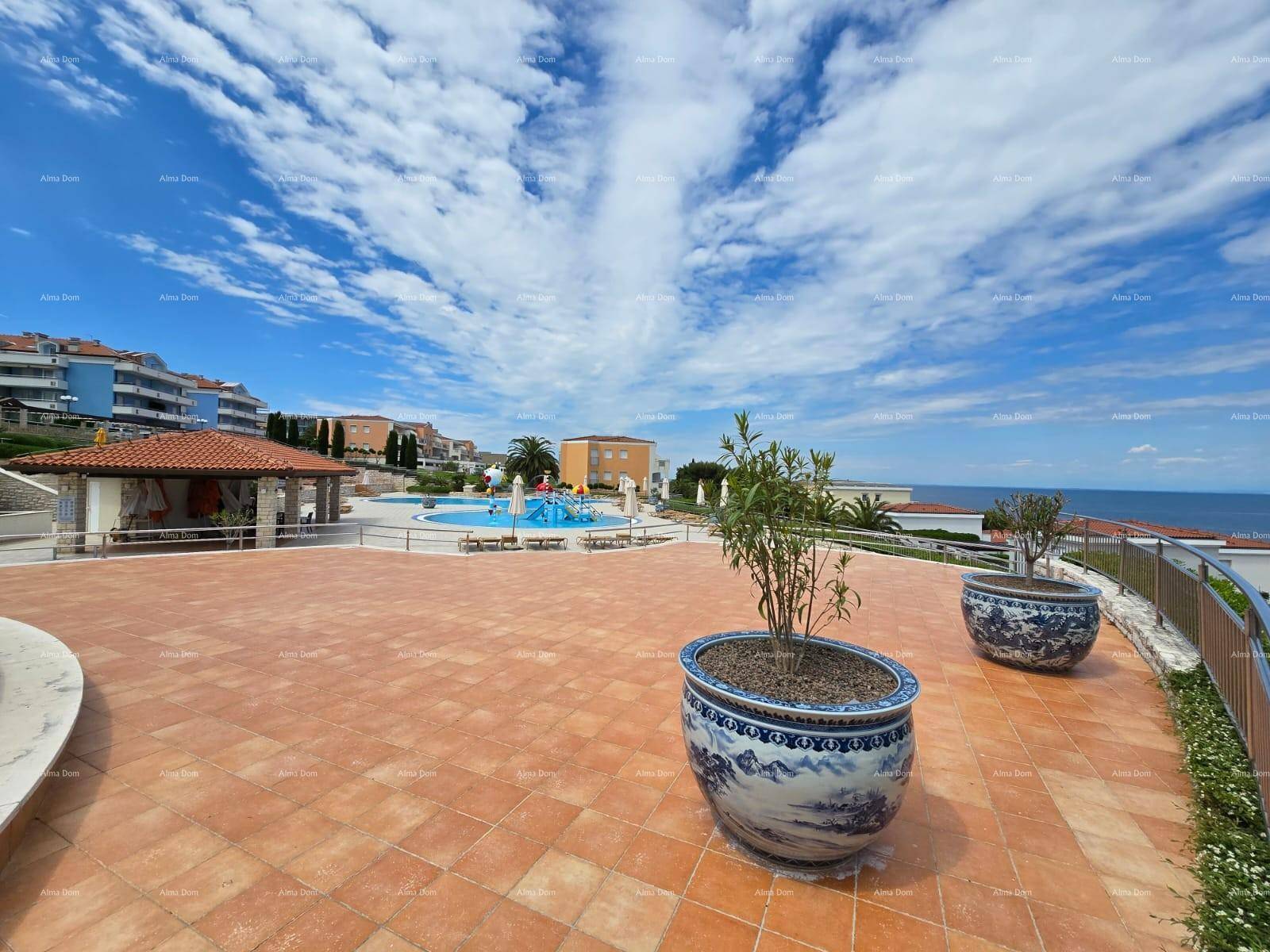Große, geflieste Terrasse mit dekorativen Pflanzen und weitem Blick auf das Meer und den Poolbereich.