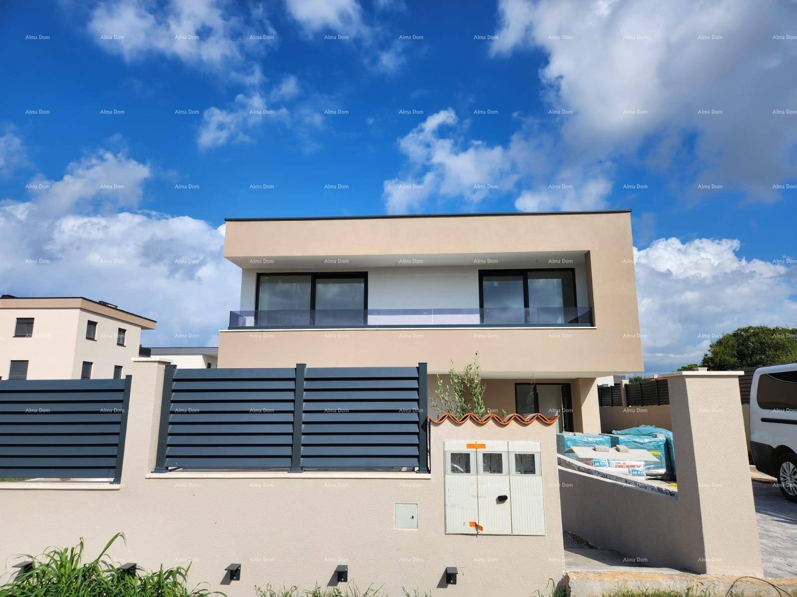 Moderne Hausfassade mit beiger Verkleidung, großen Fenstern und einem Balkon mit Glasgeländer.