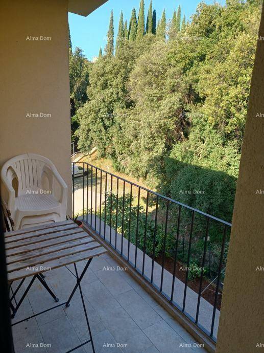 Kleiner Balkon mit einfacher Bestuhlung, umgeben von üppigem Grün und hohen Bäumen.