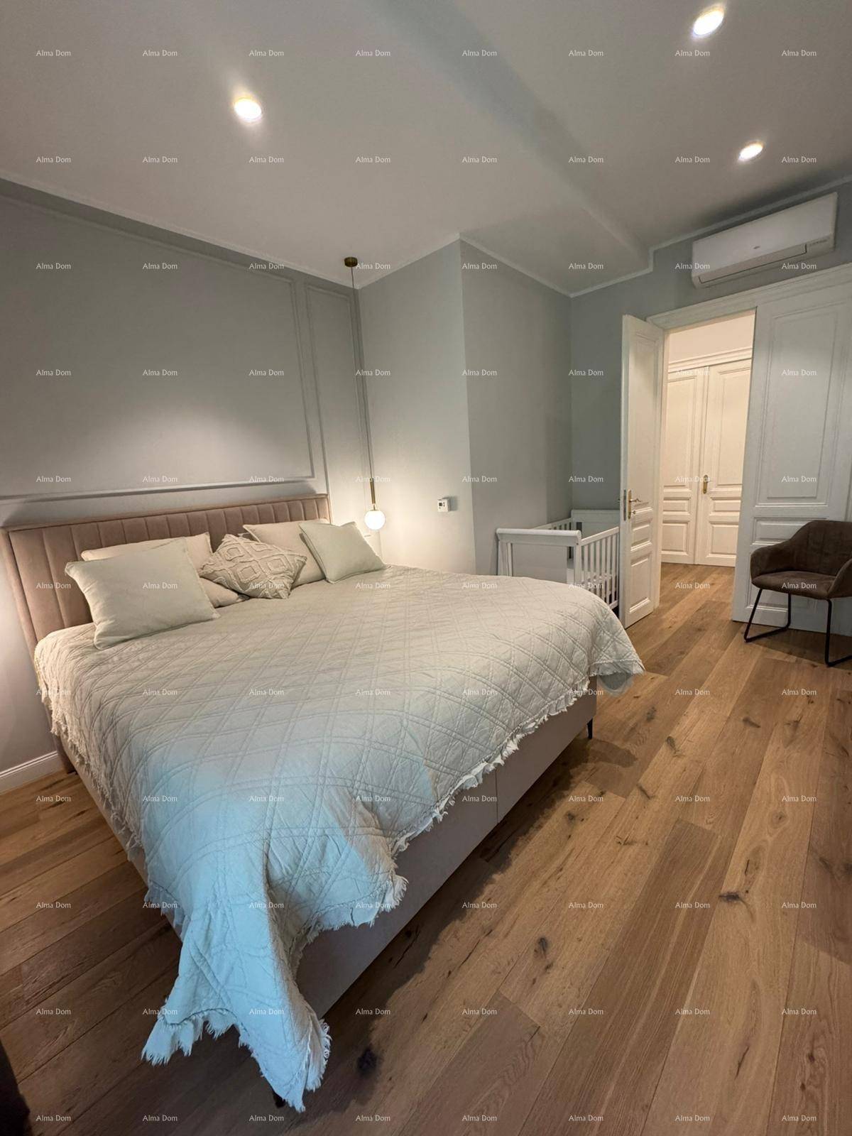 Schlafzimmer mit großem Bett, Holzboden und Babybett im Hintergrund.