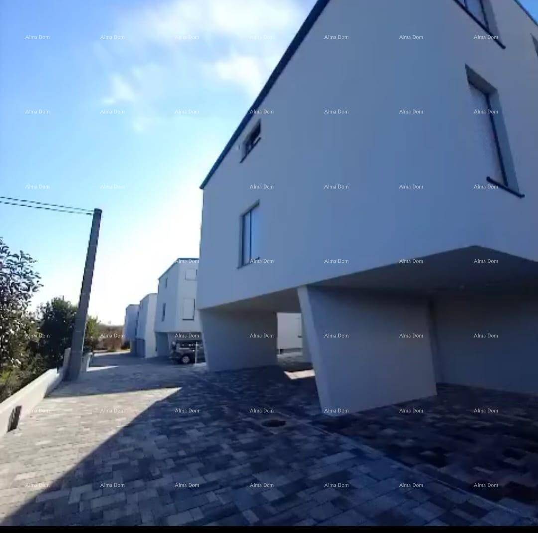 Seitenansicht eines modernen Gebäudes mit gepflasterter Zufahrt und weiteren Gebäuden im Hintergrund.