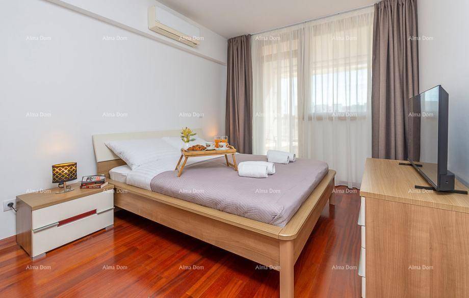 Helles Schlafzimmer mit Holzbett, Kommode und Fernseher, mit großen Fenstern und Vorhängen.