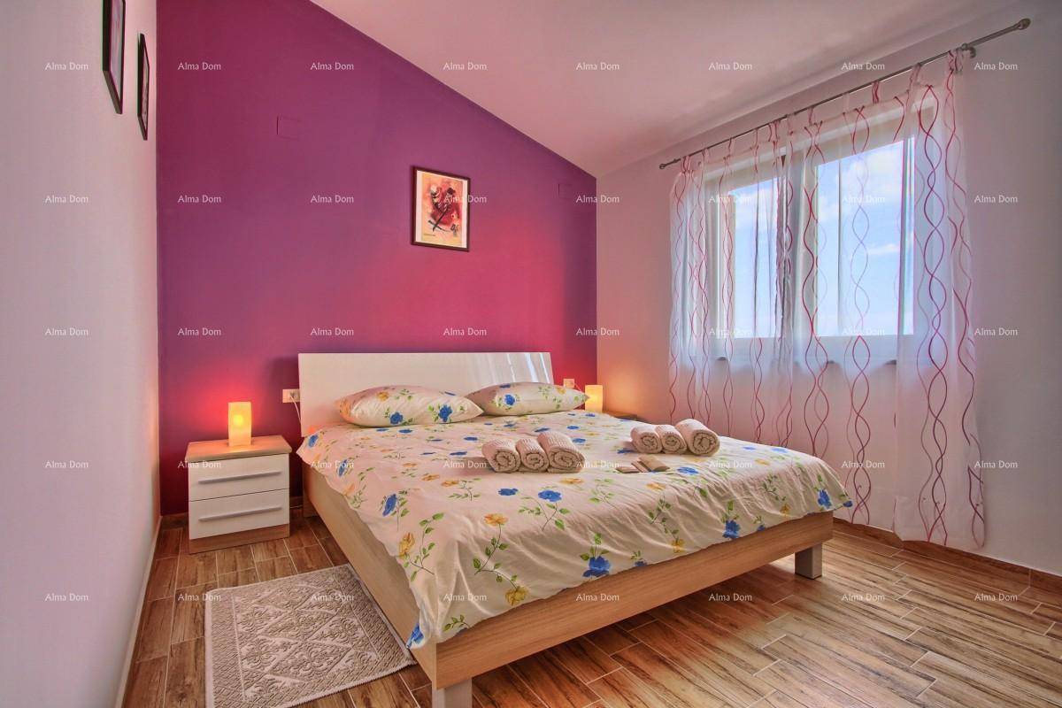 Schlafzimmer mit Doppelbett, lila Akzentwand und Fliesen in Holzoptik.