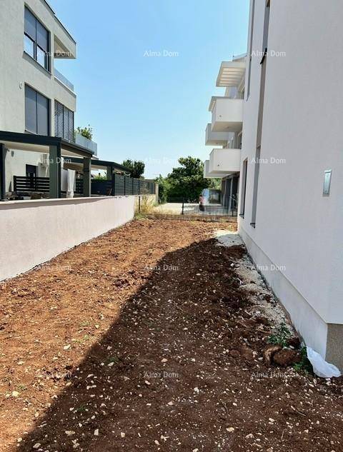 Blick entlang des Neubaus auf den unfertigen Außenbereich und weitere Gebäude in der Ferne.