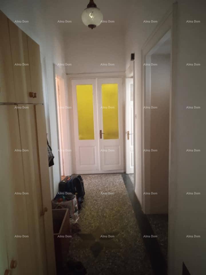 Schmaler Flur mit gemustertem Fliesenboden, Holzschrank und einer Tür mit gelben Glaseinsätzen.