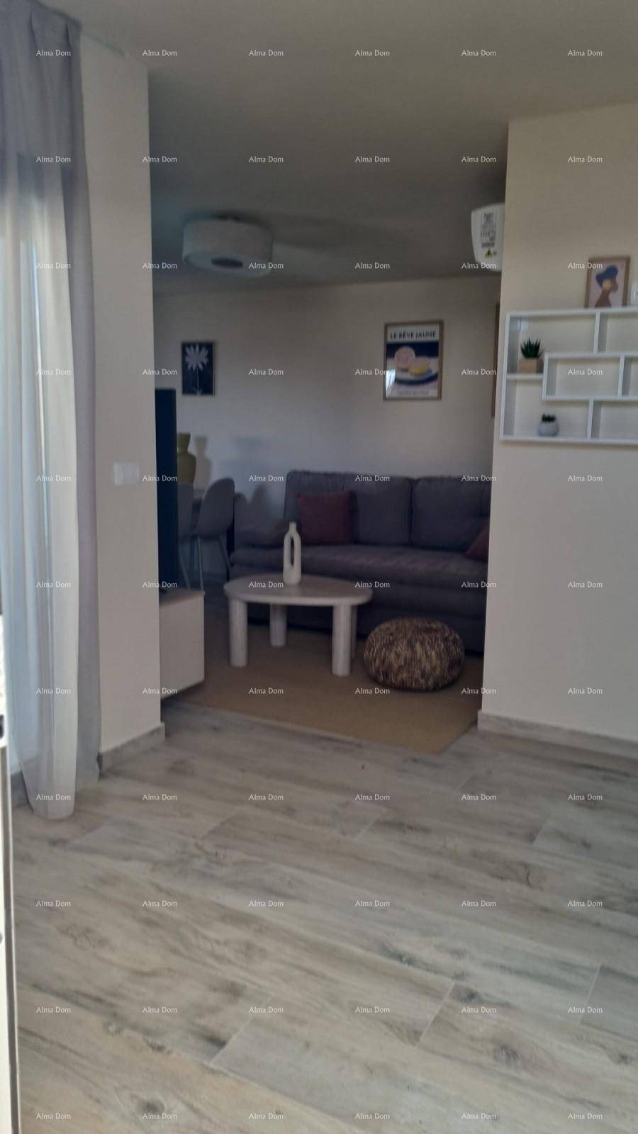 Wohnzimmer mit beigem Laminatboden, Sofa und Zugang zu einem weiteren hellen Bereich.