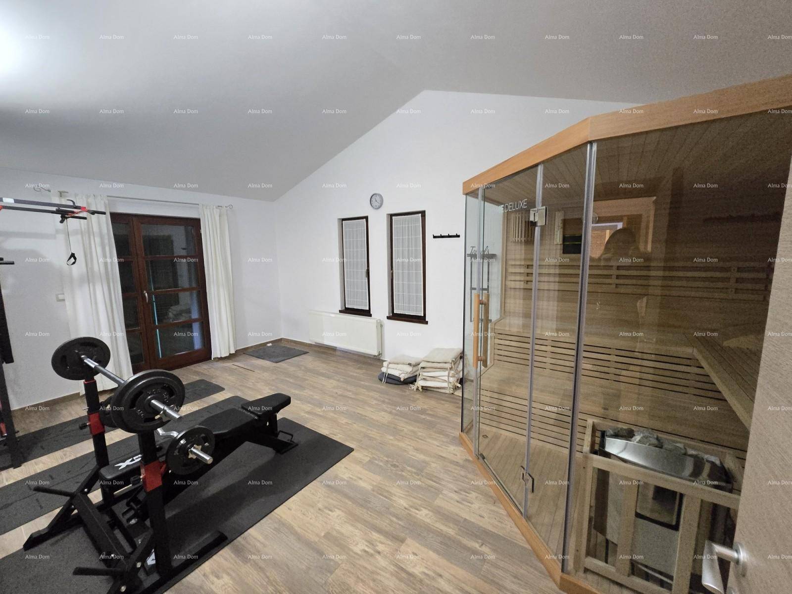 Fitnessraum mit moderner Sauna, Trainingsgeräten und Holzboden unter einer Dachschräge.