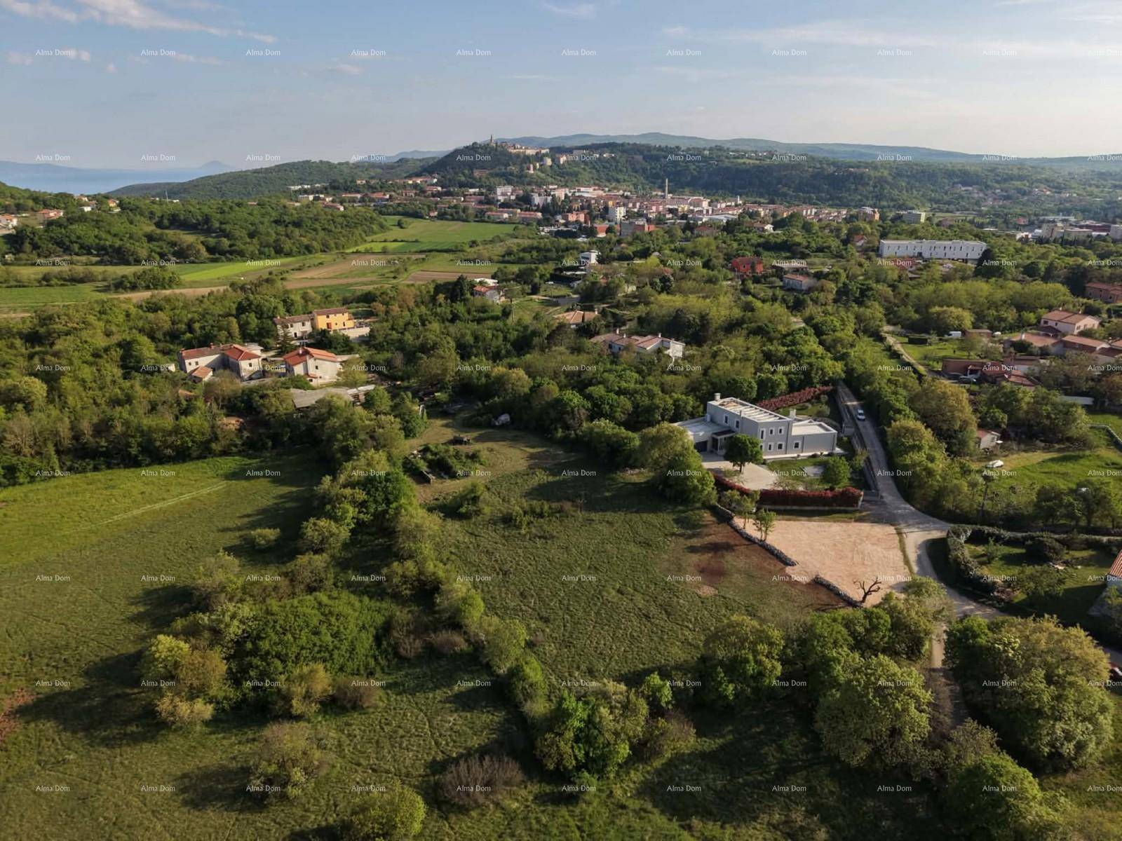 Panoramablick auf ein malerisches Dorf mit Häusern, umgeben von grünen Feldern und einem fernen Meerblick.