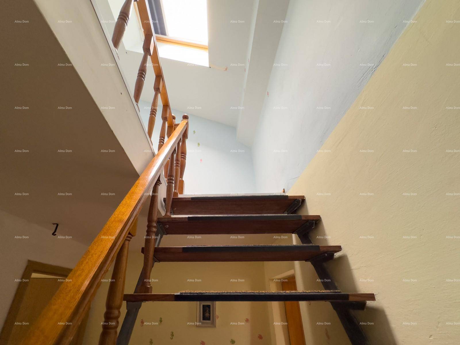 Holztreppe führt nach oben, beleuchtet durch ein Dachfenster, mit hellen Wänden.