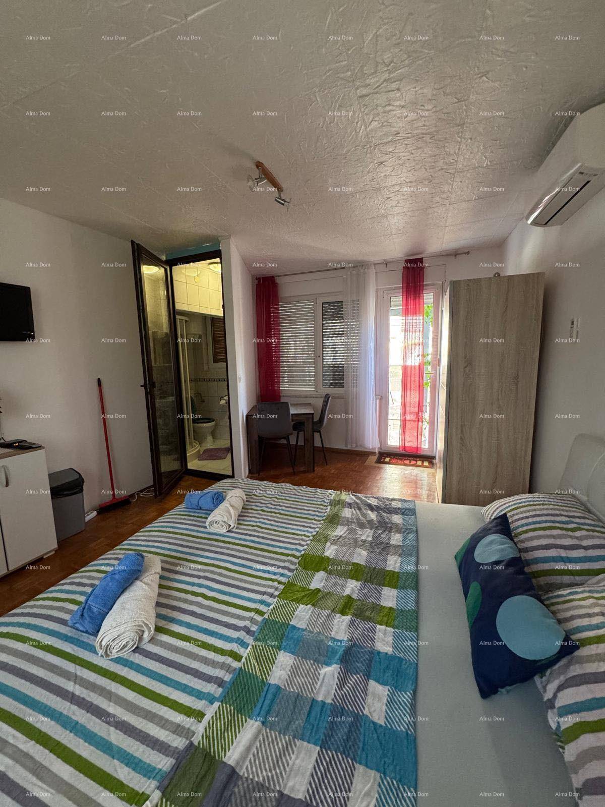 Schlafzimmer mit gestreiftem Bettzeug, Zugang zum Badezimmer und Fenster mit roten Vorhängen.